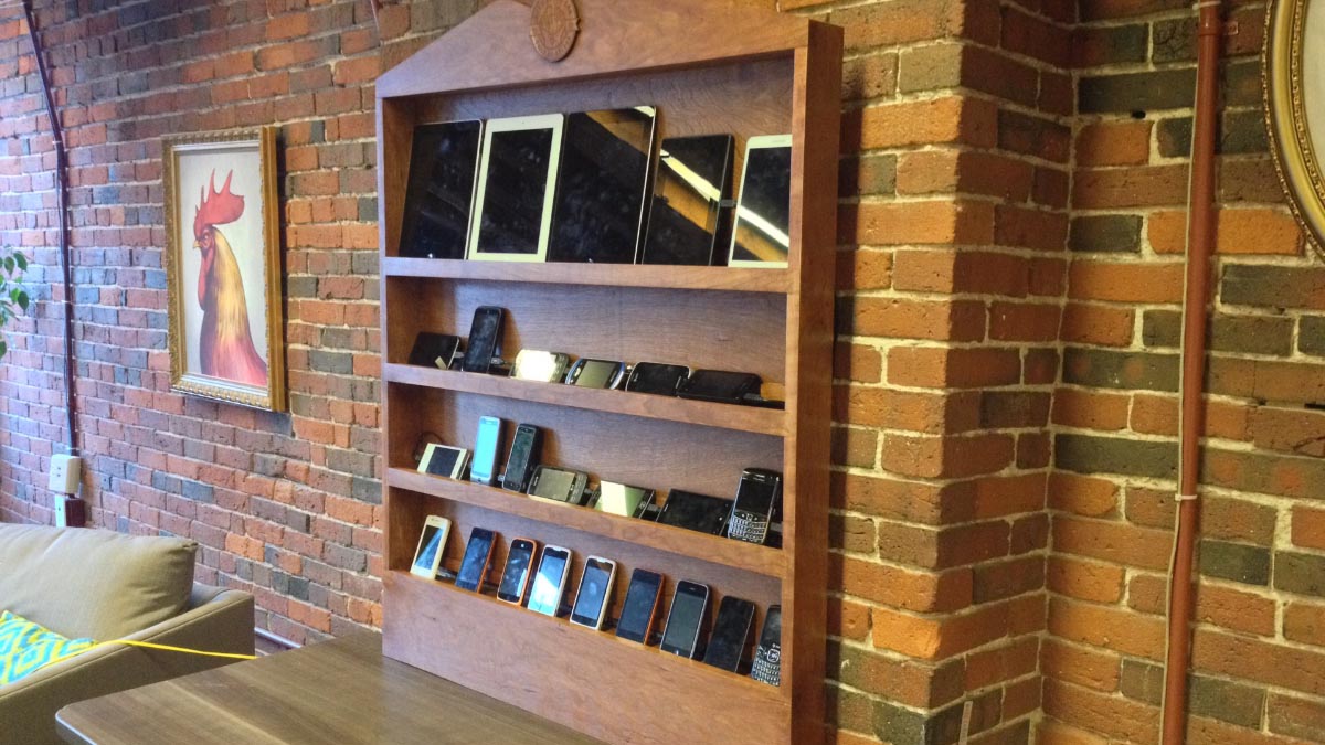 A photograph of the Bocoup Open Device Lab: a hand-made hardwood display case, with four shelves full of mobile devices and tablets.